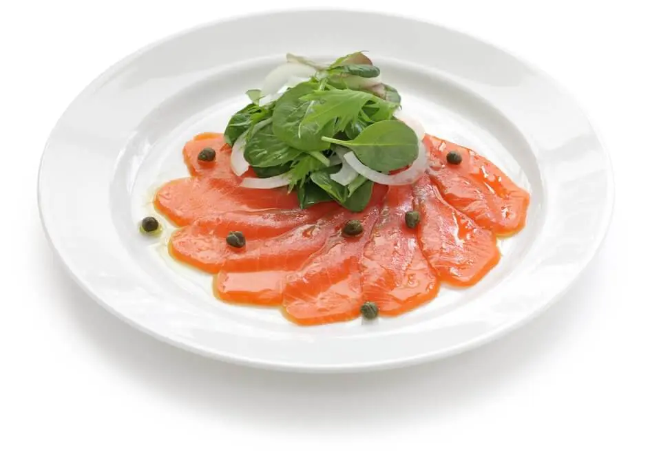 Carpaccio de saumon, présenté sous forme de coulis dans une assiette blanche, avec quelques feuilles de salade dessus.