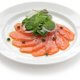 Carpaccio de saumon, présenté sous forme de coulis dans une assiette blanche, avec quelques feuilles de salade dessus.